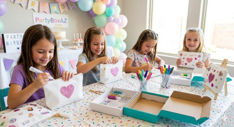May include: Four young girls are gathered around a table, engaged in a craft activity. They are decorating white canvas bags with pink heart designs using markers. The table is covered with craft supplies, including markers, stickers, and paint.