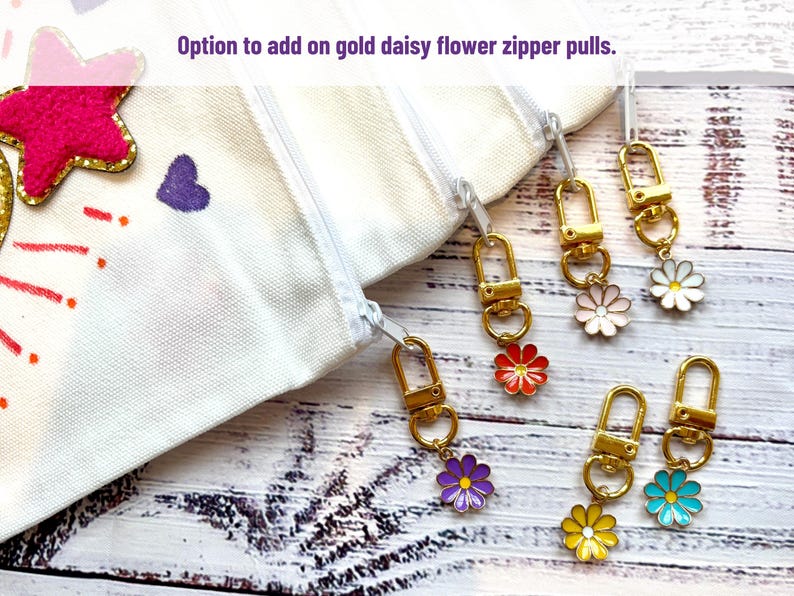 May include: White canvas zipper pouches with gold daisy flower zipper pulls in various colors. The image shows the option to add the daisy flower zipper pulls. The daisy flowers are in red, pink, white, purple, yellow, and blue.