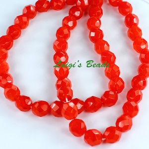 May include: Strands of faceted, bright orange beads. The beads have a geometric shape and are strung together. The text "Luigi's Beads" is visible in green. These beads are suitable for jewelry making.