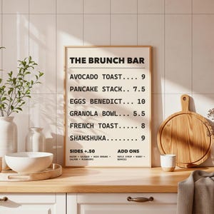 以下が含まれることがあります： 「THE BRUNCH BAR」と題された額入りのメニューボードには、アボカドトースト、パンケーキスタック、エッグベネディクトなどの朝食メニューが記載されています。 木製のまな板、小さなカップ、ボウルが木製のカウンタートップにあります。
