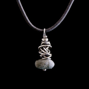 May include: A silver pendant necklace with a grey stone wrapped in silver wire. The necklace is on a black leather cord.