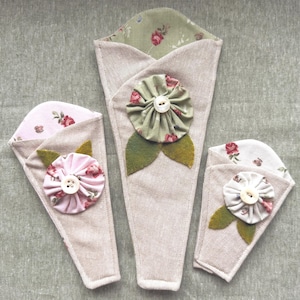 May include: Three beige fabric flower holders with floral accents. Each holder features a fabric flower with a button center and felt leaves. The interior lining of each holder has a floral pattern in pink or green.