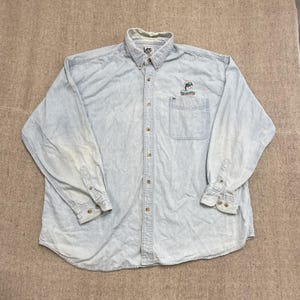 Könnte beinhalten: Hellblaues Jeans-Hemd mit Knopfleiste und langen Ärmeln. Verfügt über ein kleines gesticktes Dolphins-Logo auf der Brusttasche. Das Hemd hat einen Button-Down-Kragen und geknöpfte Manschetten. Das Lee-Markenlogo ist sichtbar.