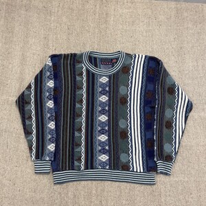 May include: A vintage crew neck sweater with a colorful geometric pattern. The sweater features vertical stripes in shades of blue, green, brown, and white. The collar, cuffs, and hem are ribbed with a striped design. The sweater has a classic, retro style.