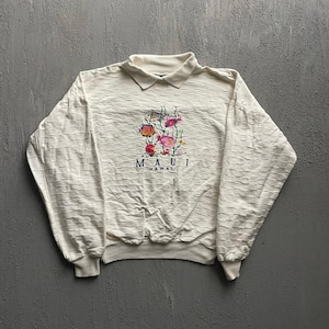 May include: An off-white long-sleeve pullover shirt with a collared neckline and a textured, horizontal brick-like pattern. The center features an embroidered graphic of colorful tropical fish and seaweed with the text MAUI HAWAII below it.