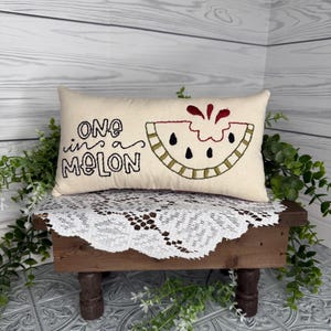 Rectangle mini pillow  6"x10" embroidered on natural muslin with "one in a melon" in black floss and a watermelon in red, two shades of green for the rind and black seeds. Backed with red ticking stipe cotton.