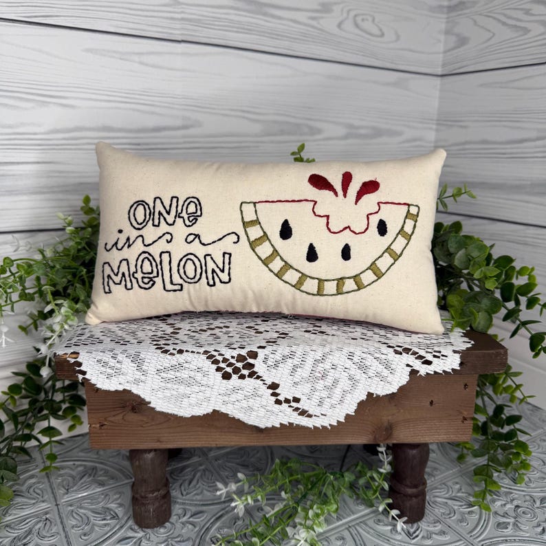 Rectangle mini pillow  6"x10" embroidered on natural muslin with "one in a melon" in black floss and a watermelon in red, two shades of green for the rind and black seeds. Backed with red ticking stipe cotton.