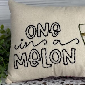 Rectangle mini pillow  6"x10" embroidered on natural muslin with "one in a melon" in black floss and a watermelon in red, two shades of green for the rind and black seeds. Backed with red ticking stipe cotton.