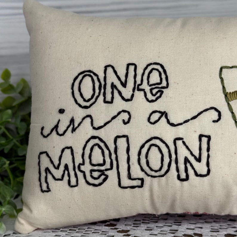 Rectangle mini pillow  6"x10" embroidered on natural muslin with "one in a melon" in black floss and a watermelon in red, two shades of green for the rind and black seeds. Backed with red ticking stipe cotton.