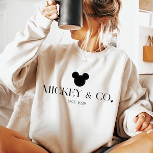 May include: A white sweatshirt with a black Mickey Mouse head and the text "Mickey & Co. Est. 1928" printed on the front.