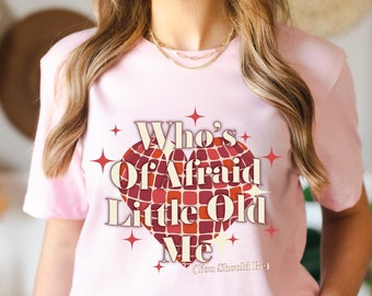 May include: Pink t-shirt with a red heart graphic that says "Who's Afraid of a Little Old Me (You Should Be)".