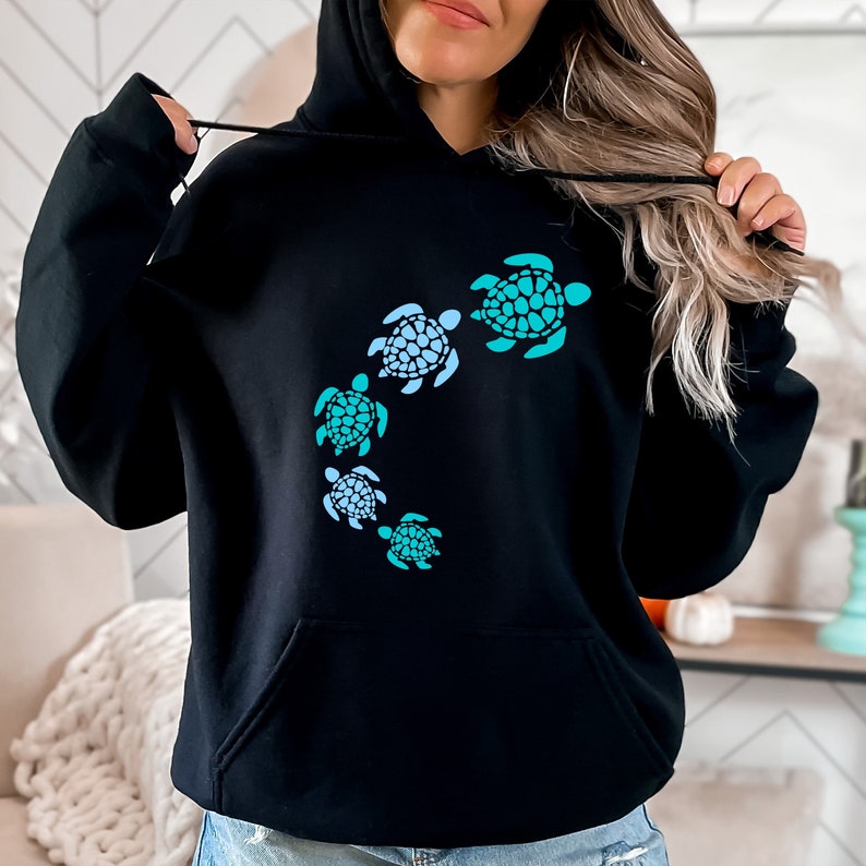 K&ouml;nnte beinhalten: Schwarzer Kapuzenpullover mit einem Aufdruck von f&uuml;nf blauen und gr&uuml;nen Meeresschildkr&ouml;ten, die im Kreis schwimmen.