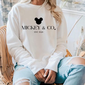 May include: White sweatshirt with a black Mickey Mouse head and the text "Mickey & Co. Est. 1928" printed on the front.