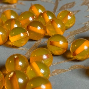 May include: A collection of amber glass beads with a translucent orange stripe running through the center of each bead.