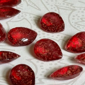 May include: A collection of red teardrop-shaped glass beads with a sparkly finish.