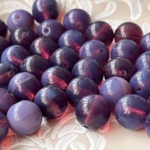 May include: A collection of round, iridescent purple beads. The beads have a smooth, glossy finish and are perfect for jewelry making.
