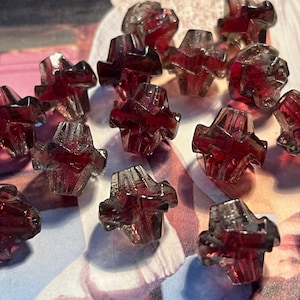 May include: A collection of 15 small, clear glass beads with a deep red hue. The beads are faceted and have a starburst design.