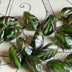 May include: A collection of green glass beads with gold flecks. The beads are teardrop shaped and have a glossy finish.