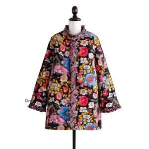 May include: A floral print coat with a black background, featuring a vibrant array of pink, blue, yellow, and white flowers. The coat has a ruffled collar and trim, and is displayed on a mannequin. The coat's length is mid-thigh.
