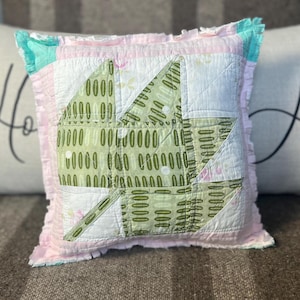 May include: A pink and green patchwork pillow with a ruffled edge. The pillow is made of different fabrics with a green and white pattern.