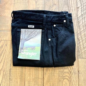 May include: Black Wrangler jeans with a white label that says "26 MWZ Wrangler, Button Fly, Original Fit".