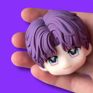 Pode incluir: Uma pequena cabeça de estatueta em estilo anime, com cabelo roxo e olhos grandes e expressivos. A estatueta tem uma tez pálida e um sorriso suave. O fundo é de cor roxa sólida.