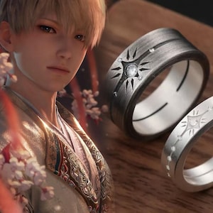 May include: Two silver rings with a starburst design and small clear stones. The rings are on a wooden surface.