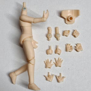 May include: A disassembled, light tan action figure with multiple interchangeable hand and arm pieces. The figure's body is articulated at the joints, and the head is separate. Additional parts include a neck piece and two arm attachments.