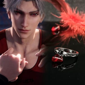 May include: A black ring with a large black gemstone and smaller white gemstones set in a silver band. The ring is on a red surface.