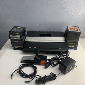 May include: A white ceramic mug with a black handle and the text "But First, Coffee" in a black, handwritten-style font. The mug is on a white surface.