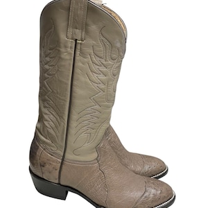 May include: A pair of tan cowboy boots. The boots have a textured toe and a smooth shaft with decorative stitching. The heels are black, and the soles have a white trim. The boots are made of leather.