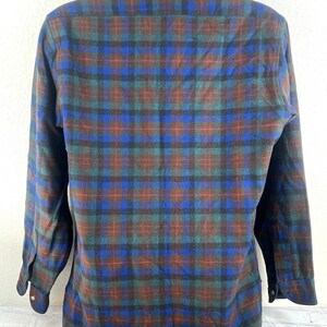 May include: A long-sleeve button-down shirt featuring a plaid pattern in shades of blue, dark green, and red. The shirt has a standard collar, buttoned cuffs, and a straight hemline. The fabric displays a soft, brushed texture throughout the garment.