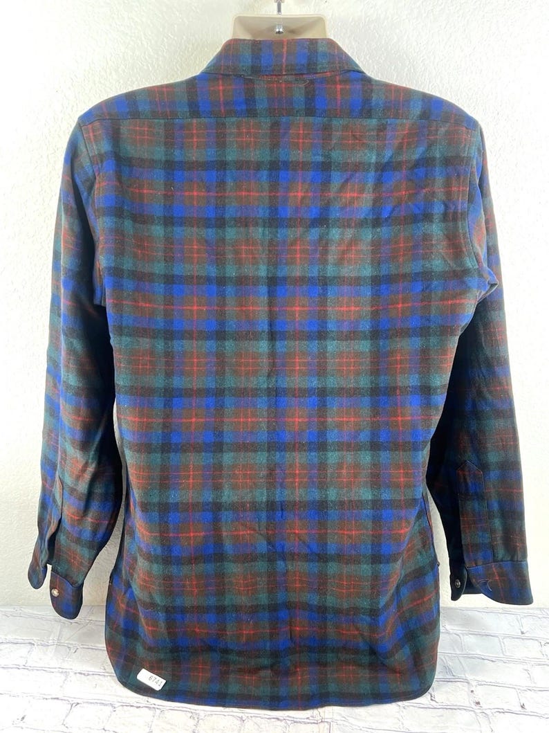 May include: A long-sleeve button-down shirt featuring a plaid pattern in shades of blue, dark green, and red. The shirt has a standard collar, buttoned cuffs, and a straight hemline. The fabric displays a soft, brushed texture throughout the garment.