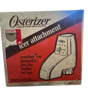 Peut inclure: Boîte d'accessoire à glace Osterizer vintage. La boîte est beige et rouge avec les mots "Osterizer Liqueifier-Blender" et "ice attachment". La boîte présente un dessin au trait de l'accessoire à glace et le texte "crushes ice instantly for the buffet or bar".