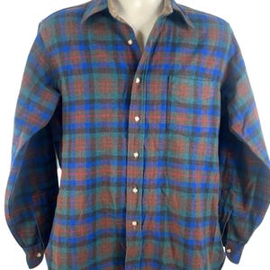 May include: A long-sleeve button-down shirt featuring a plaid pattern in shades of blue, green, and red. The shirt has a standard collar, a single chest pocket on the left side, and light-colored buttons running down the front placket and on the cuffs.