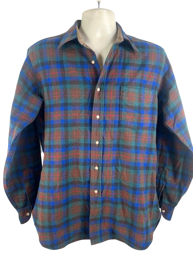 May include: A long-sleeve button-down shirt featuring a plaid pattern in shades of blue, green, and red. The shirt has a standard collar, a single chest pocket on the left side, and light-colored buttons running down the front placket and on the cuffs.