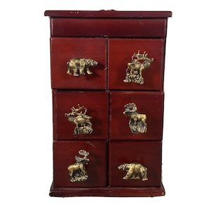 Könnte beinhalten: Eine rote Holzkiste mit sechs Schubladen. Jede Schublade hat einen anderen tierförmigen Messinggriff: einen Bären, einen Elch, einen Elch, einen Hirsch und zwei weitere Elche.