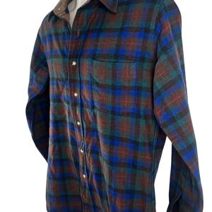 May include: A long-sleeve button-down shirt featuring a plaid pattern in shades of blue, green, brown, and black. The shirt has a pointed collar, a single chest pocket on the left side, and light-colored buttons running down the front placket.