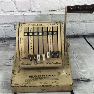 May include: A vintage white cash register with a black handle. The register has a display with the words "DOLLARS" and "CENTS" and a series of numbers. The register also has a warning label that reads "BEWARE OF UNAUTHORIZED PERSONNEL".