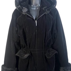 May include: A black velvet hooded coat with a faux fur trim on the hood and cuffs. The coat has a zipper closure and two front pockets. The waist is cinched with a drawstring. The coat is hanging on a black hanger.