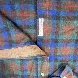 May include: A long-sleeve shirt featuring a Macduff Hunting tartan pattern in shades of blue, green, black, and red. The shirt includes a tan inner collar lining, light-colored buttons, and a white fabric label reading AUTHENTIC MACDUFF HUNTING TARTAN.
