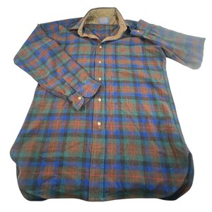May include: A long-sleeve button-down shirt featuring a plaid pattern in shades of blue, green, and brown. The shirt includes a tan quilted collar, a single chest pocket, and a front button closure with light-colored buttons on the placket and cuffs.