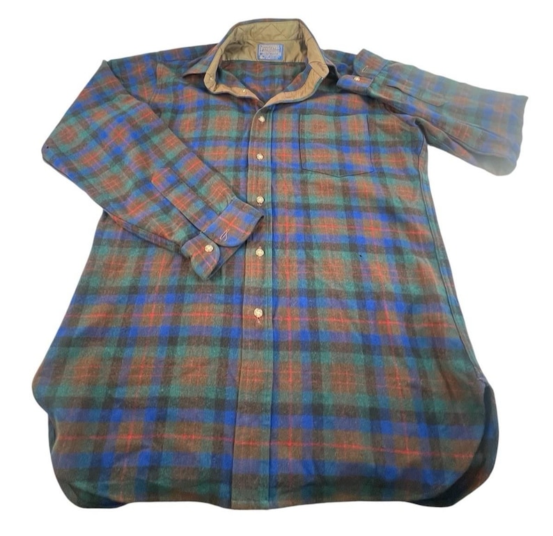 May include: A long-sleeve button-down shirt featuring a plaid pattern in shades of blue, green, and brown. The shirt includes a tan quilted collar, a single chest pocket, and a front button closure with light-colored buttons on the placket and cuffs.