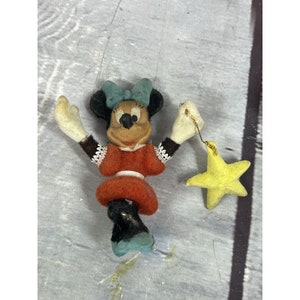 May include: A vintage plush Minnie Mouse figurine with a red dress, black shoes, and a blue bow. She is holding a yellow star with a gold string.