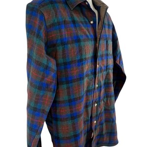 May include: A long-sleeve button-down shirt featuring a plaid pattern in shades of blue, green, and brown. The shirt has a pointed collar, a single chest pocket, and light-colored buttons running down the front placket. The interior collar lining is brown.