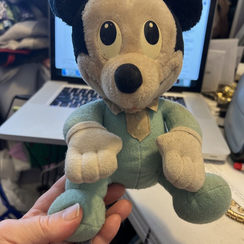 May include: A vintage plush Mickey Mouse toy wearing a light blue sleeper with white trim. The toy has large, black eyes and a black nose.