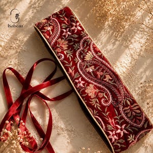 Peut inclure: Une ceinture rectangulaire en velours rouge profond ornée de broderies florales et cachemire complexes dans des tons rose, vert et crème. L'accessoire comprend de longs rubans en velours rouge assortis pour la fixation et le logo Isabeau.