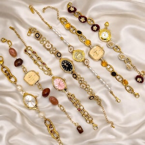 May include: A collection of gold-coloured watches with diverse strap designs. The watches have oval, square, and round faces, in colours such as white, black, and pink. Some straps incorporate pearls, beads, and decorative links.