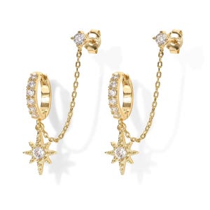 May include: A pair of gold-tone earrings featuring a small hoop encrusted with clear stones, connected by a delicate chain to a star-shaped charm with a central clear stone, and a matching stud post at the top with a single clear stone.