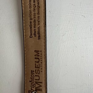 Puede incluir: Primer plano del interior de un cintur&oacute;n de cuero marr&oacute;n con el texto "Brighton MUSEUM collection". El interior del cintur&oacute;n tambi&eacute;n presenta el texto: "Monedas de oro decorativas, particularmente a menudo convertidas en anillos y premiadas por la tradici&oacute;n, hemos dise&ntilde;ado las nuestras."